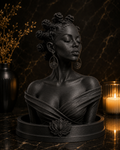 A dark matte black sculpture of a woman's bust with bantu knots , wearing draped fabric and large lotus earrings, displayed on a circular base with a lotus emblem. The bust is set on a polished dark marble surface with a lit candle and a vase of dried branches in the background.