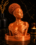 A metallic bronze bust sculpture of a woman with closed eyes and an elegant high bun hairstyle, displayed on a matching circular base with a lotus flower detail, set against a dark marble background with decorative vases and a candle.